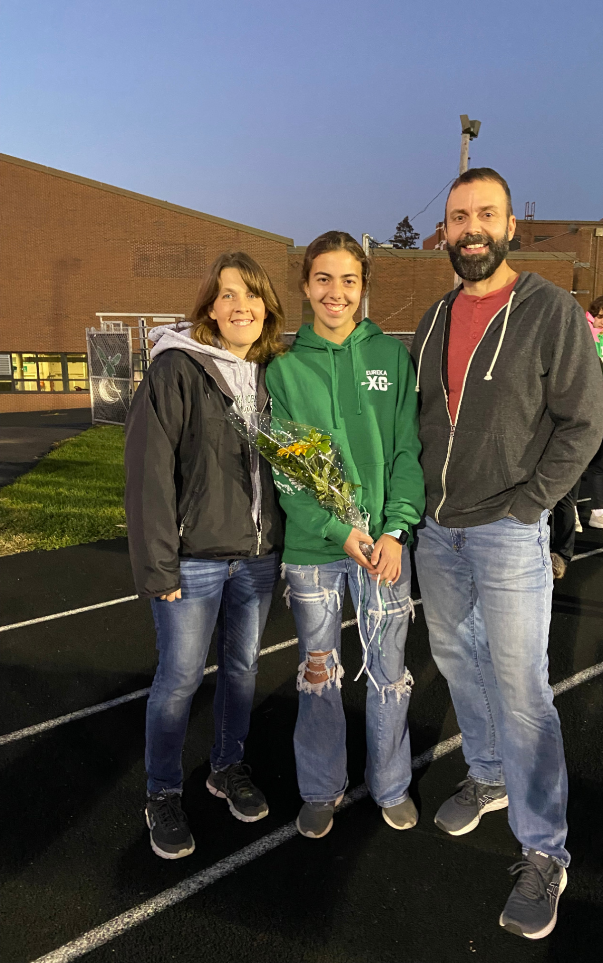 a girl, mom and dad on senior night on a high school track. 